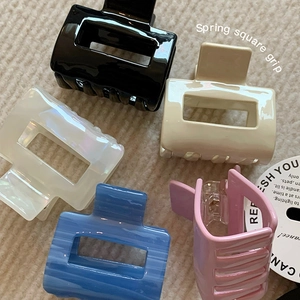 Close-up of five square acetate hair claws in various marble colors on a knit surface