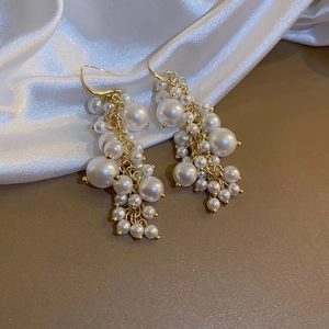 Detailed view of cluster pearl fringe earrings with golden hooks on white silk fabric