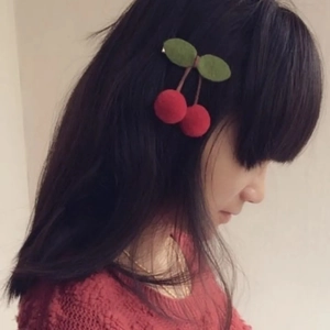 Detail of red cherry hair clip with green leaves worn on a girl's hair for a cute style