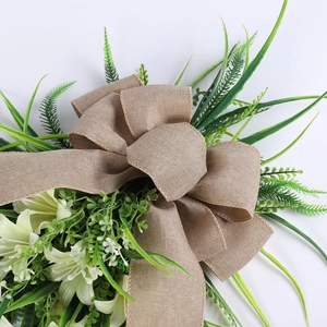 Detail view of rustic burlap bow and green foliage on a decorative lily teardrop wreath