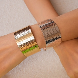 Detailed view of irregular hammered metal wide open bangles in gold and silver finish