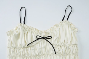Detail of white satin camisole featuring black shoulder straps and a delicate bow tie