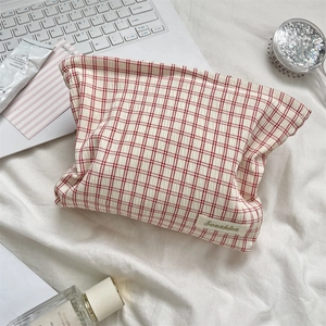 Macro shot of red plaid cosmetic bag with brand woven label on white bedding