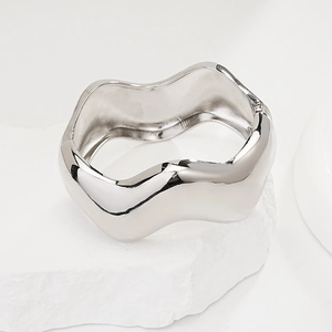 Detail of silver wavy irregular cuff bracelet on white stone textured pedestal