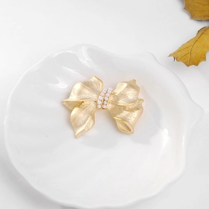 Detailed view of golden bow brooch with brushed texture and delicate white pearls
