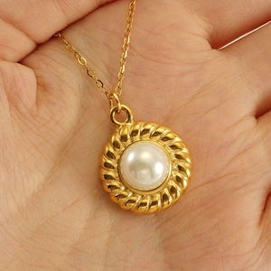 Macro shot of 18k gold-plated twisted rope pendant with a white pearl on a hand
