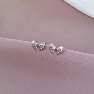 Close-up of silver bow stud earrings on soft purple silk fabric for elegant style