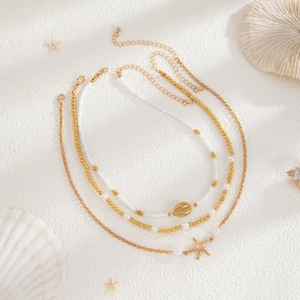 Detail of layered gold necklace with white beads, starfish charms and shell pendants