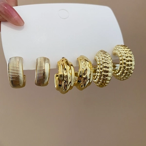Detailed close-up of three gold C-shaped earrings with textured patterns on a display card
