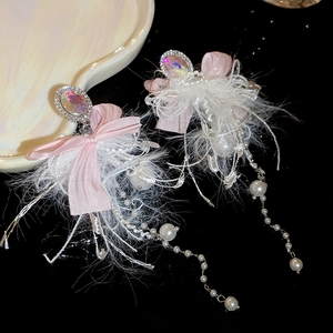 Detailed view of pink bow earrings with rhinestones, long white feathers and pearl tassels