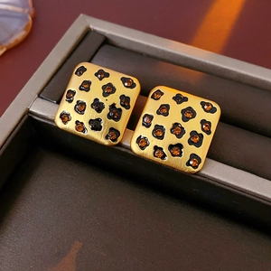 Macro shot of square gold leopard print earrings with orange crystals in a jewelry box