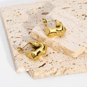 Detailed view of irregular pleated V-shaped gold earrings on textured stone props