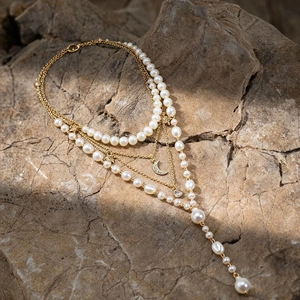 Detail of layered gold necklace with moon and star charms on natural stone