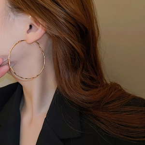 Close-up of a model wearing large golden geometric hoop earrings in a warm studio setting