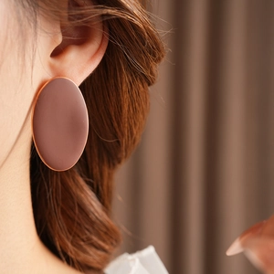 Dettaglio di un orecchino ovale opaco color terracotta indossato da una modella