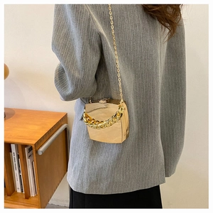 Chic gold metallic clutch bag with thin chain strap shown on a gray blazer outfit