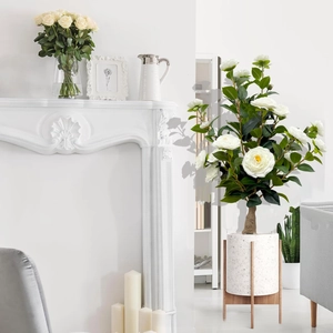 Minimalist white artificial camellia plant in a marble pot with a wooden tripod stand