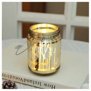 Detail view of a glass jar lantern with reindeer forest pattern and warm LED lights inside