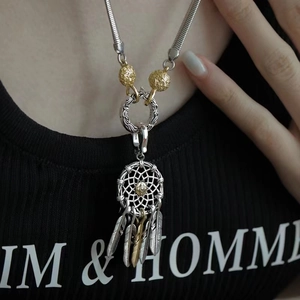 Close-up of a two-tone dreamcatcher pendant necklace on a model with gold feather accents