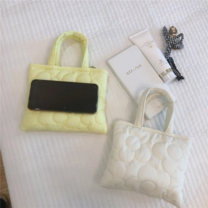 Mini borsa trapuntata a fiori gialla e crema con accessori quotidiani sul letto