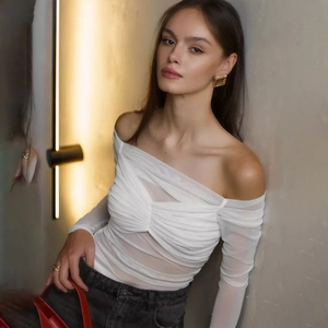 Detail of off-shoulder white mesh top paired with dark denim and golden earrings