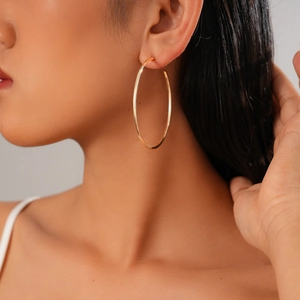 Close-up of a large gold minimalist hoop earring worn by a model in a side view