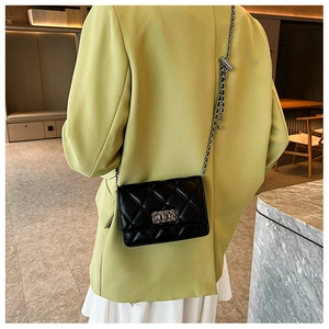Close-up of black quilted crossbody bag with silver chain strap and metal clasp on green blazer