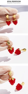 Detail presentation showing handmade red raspberry earrings with gold metal and green leaf