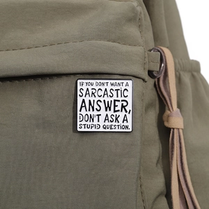 Gros plan d'un pin's carré en émail avec texte sur le fond d'un sac en toile verte