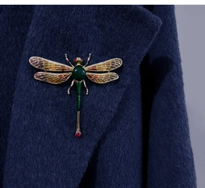 Detailed close-up of a large dragonfly brooch with green enamel and gold metal finish