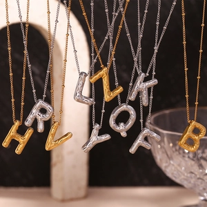 Detail van 18K goud en zilveren ballonletterhangers met opgeblazen textuur aan een kralenketting