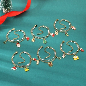 Flat lay of six double-layer Christmas charm bracelets with enamel pendants on green surface