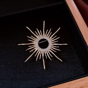Macro shot of sunburst gold plated brooch with white zircon on black velvet padding