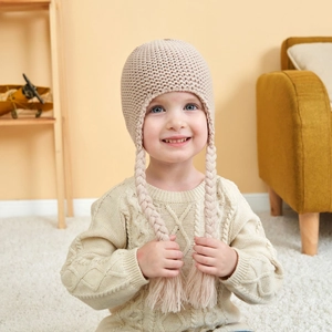 Detail of baby knit hat featuring braided wig tassels and warm fleece lining in beige
