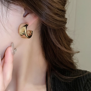 Gros plan de boucles d'oreilles dorées en forme de C portées par un mannequin avec soin