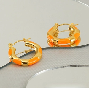 Close-up of golden titanium hoop earrings with orange enamel segments on a reflective surface