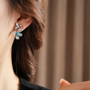 Close-up of a silver butterfly earring with blue stone and crystals on a model's ear