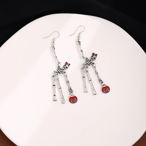 Macro detail of skeleton earrings featuring silver skull frames and red pumpkin charms