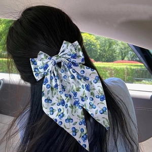 Detailed view of blueberry print bow hair clip with long ribbons on dark hair