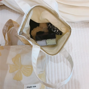 Detail of canvas mini bag showing yellow bow jacquard, zipper closure and inner space
