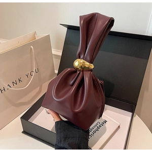 Macro shot of burgundy faux leather pleated handbag with gold ring handle and gift box