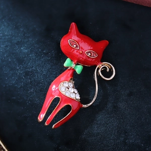 Enamel red cat brooch with green bow and white crystals on a navy textured surface