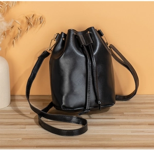 Close-up of black PU leather drawstring bucket bag with gold hardware on wooden table