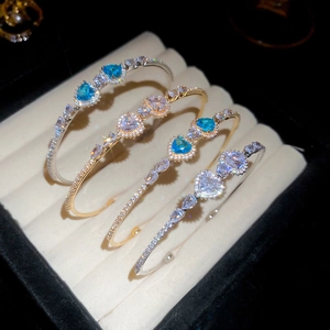 Macro display of four luxury zircon heart-shaped open bangles in gold and silver plating