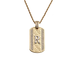 Détail d'un pendentif doré rectangulaire avec lettre R en cristal et chaîne torsadée