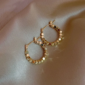 Detail of gold beaded hoop earrings resting on elegant champagne silk fabric background