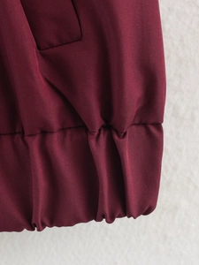 Détail de la manche d'une veste rouge foncé avec poignet élastique et texture tissée