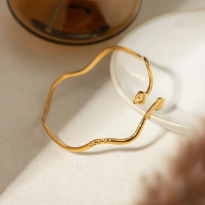 Polished 18k gold stainless steel wavy snake cuff bracelet on a white ceramic plate