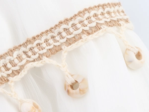 Detailed view of bohemian style macrame fringe with shell beads on a white cotton fabric