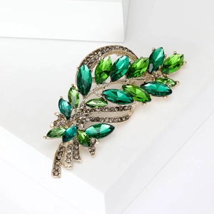 Macro shot of elegant wheat stalk brooch featuring emerald green crystals on gold metal